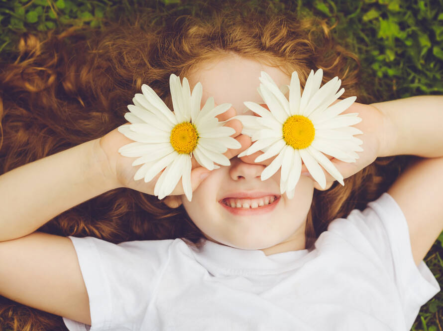 Lächelndes Kind mit Blumen auf den Augen